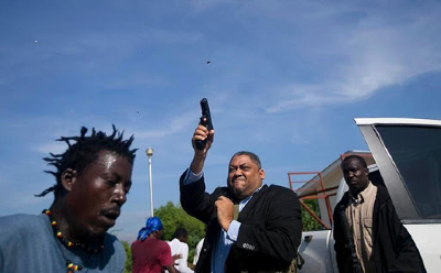 Ruling party Senator Ralph Fethiere fires his gun outside Parliament as he arrives for a vote on the ratification of Fritz William Michel's nomination as prime minister in Port-au-Prince, Haiti, Monday, Sept. 23, 2019. Opposition members confronted ruling-party senators, and Fethiere pulled a pistol when protesters rushed at him and members of his entourage. The vote was cancelled. (AP Photo/Dieu Nalio Chery)